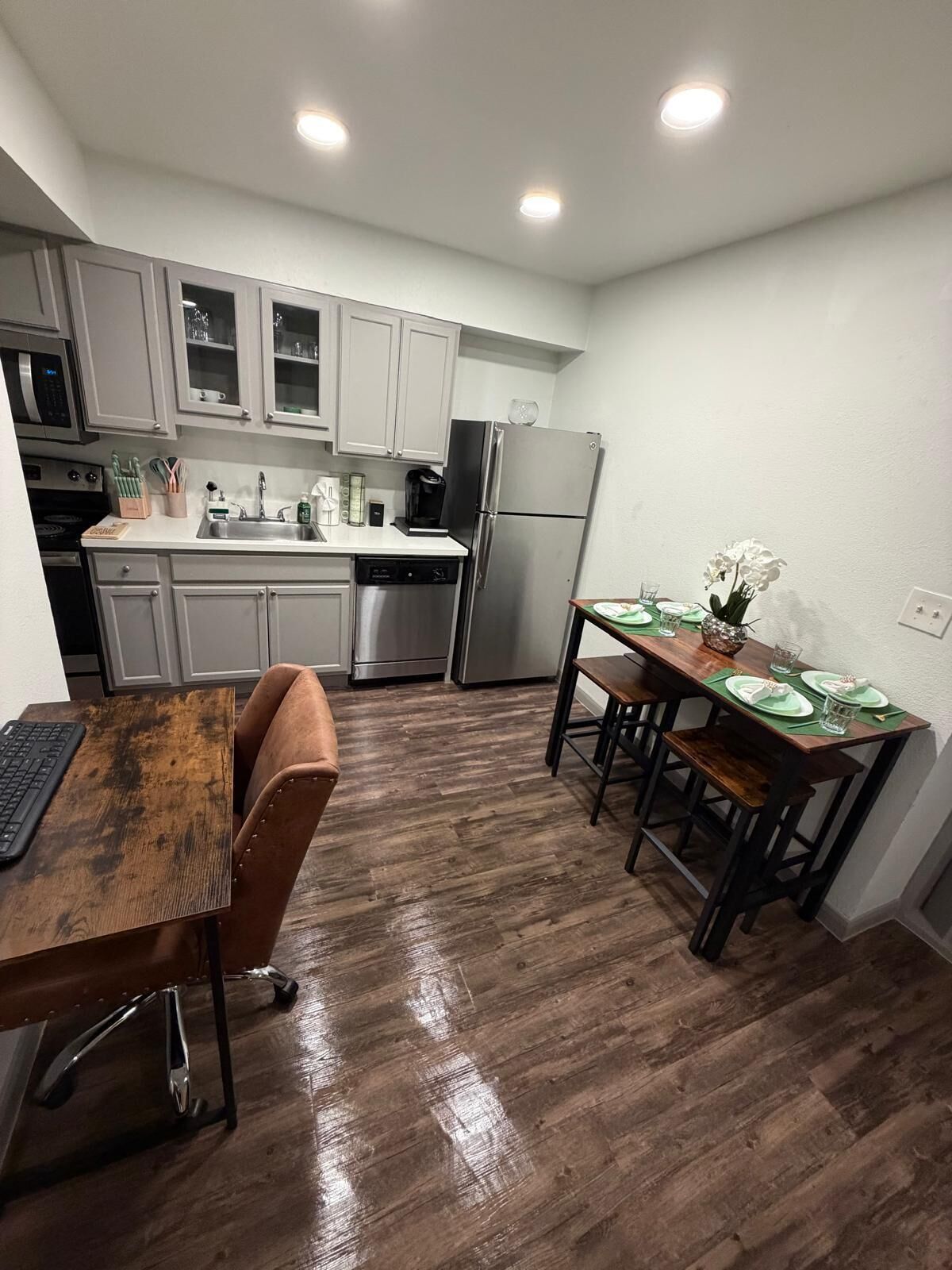 Cocina compacta con armarios blancos, electrodomésticos de acero inoxidable y una zona de comedor con mesa y sillas de madera.
