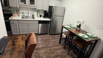 Cocina compacta con armarios blancos, electrodomésticos de acero inoxidable y una zona de comedor con mesa y sillas de madera.