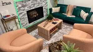 A living room with a fireplace, green sofa, two armchairs, a coffee table, and a TV mounted on the wall. - Modern Studio Apartment Pool & Gym Access Ideal for Relaxing Stays in Houston (Houston)