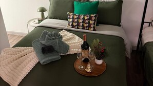 A neatly arranged bedroom with a green bedspread, a decorative wall piece, a small bedside table with a lamp, and a tray with glasses and a bottle. - Modern Studio Apartment Pool & Gym Access Ideal for Relaxing Stays in Houston (Houston)
