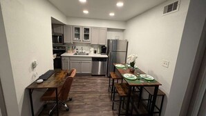 A compact kitchen with modern appliances, a dining table set for four, and a small office area with a desk and chair. - Modern Studio Apartment Pool & Gym Access Ideal for Relaxing Stays in Houston (Houston)