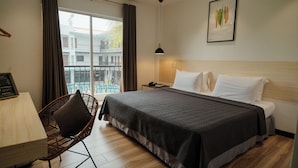 Une chambre d’hôtel avec un lit, une chaise, une table de chevet, une lampe, une fenêtre avec des rideaux et une vue sur les bâtiments environnants.