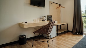Une chambre d’hôtel moderne avec un bureau en bois, un téléviseur fixé au mur, un porte-manteau suspendu et une vue sur l’extérieur.
