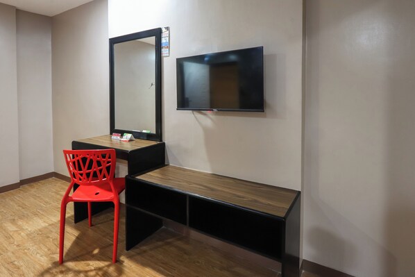 Une pièce avec un bureau en bois, une chaise rouge, un grand miroir et un téléviseur à écran plat fixé au mur.