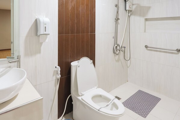 Un bagno moderno con il water, un erogatore di sapone, una doccia e una barra di sostegno.