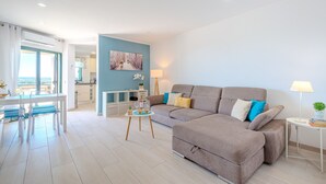 Un soggiorno moderno con un divano, un tavolo da pranzo con sedie e una zona cucina sullo sfondo.