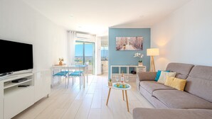 Un soggiorno moderno con una TV a schermo piatto, un divano, un'area pranzo con tavolo e sedie, e una cucina sullo sfondo.