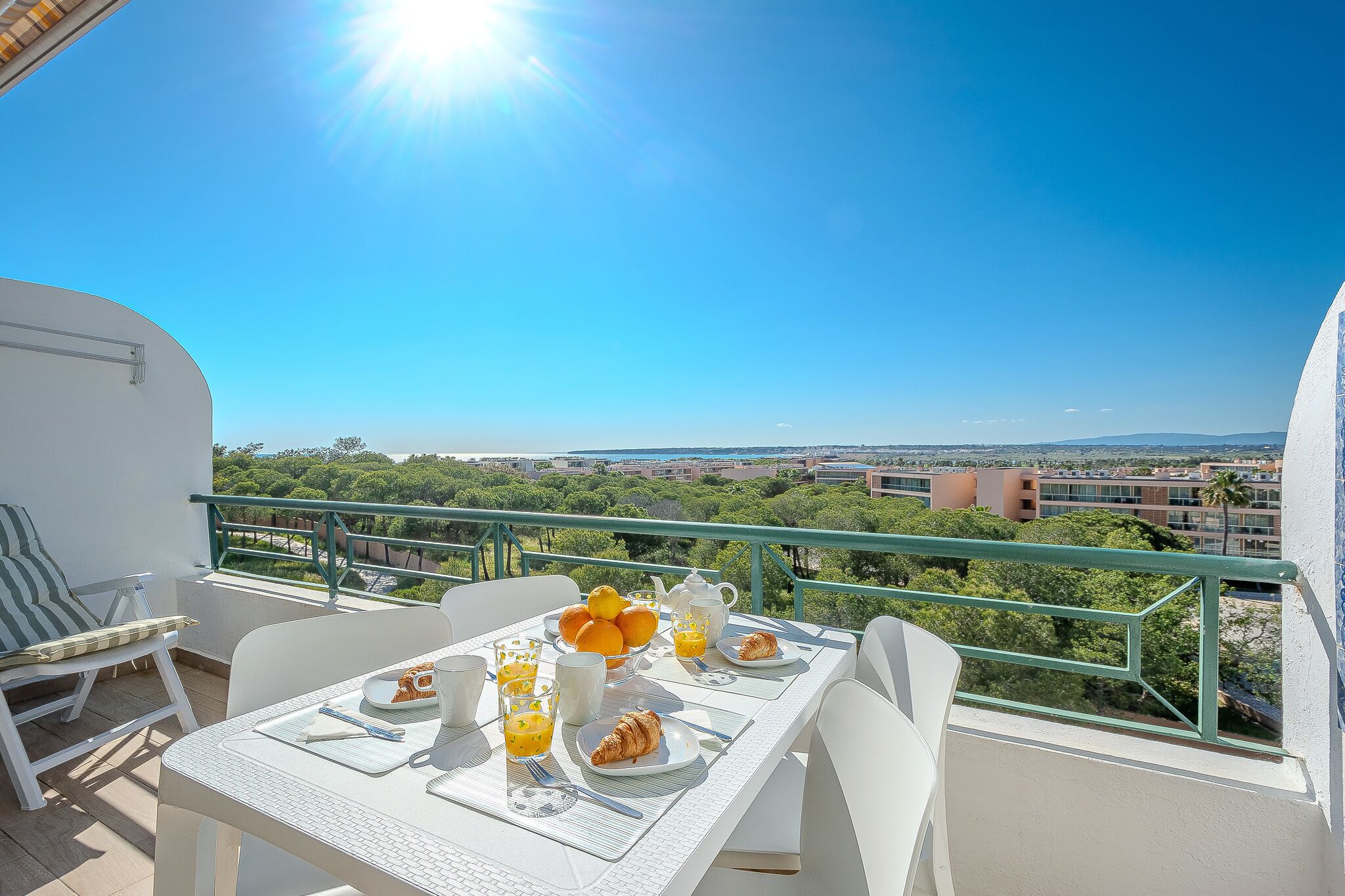 Ein Balkon mit Frühstückstisch, einem Stuhl und Blick auf die Stadt und Grünflächen.