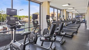 Un gimnasio con bicicletas estáticas y cintas de correr, ventanas amplias y vistas al exterior.