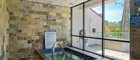 Ein Wellnessbereich mit Steinwand, einem Schild mit Spa-Regeln, einem Pool und Blick ins Freie.