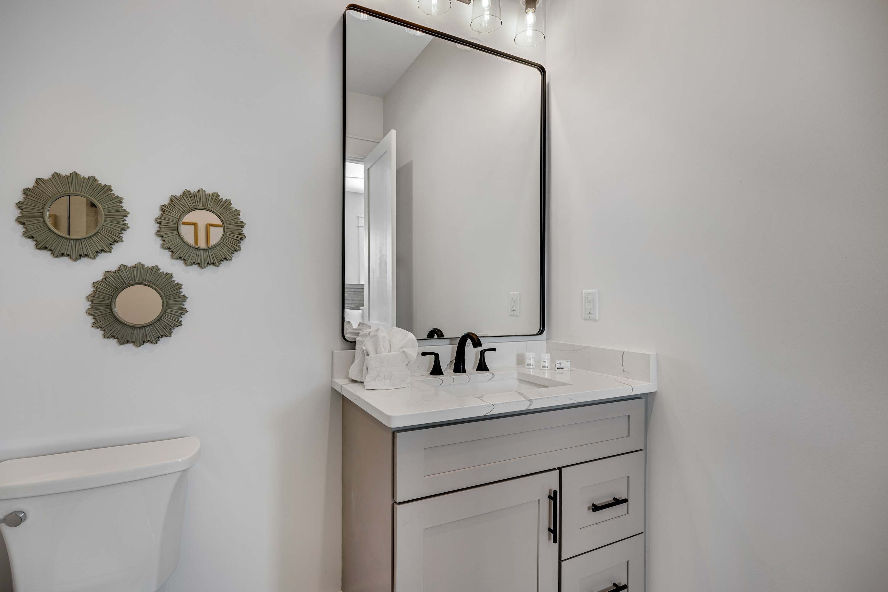 Une salle de bain comprenant des toilettes, un lavabo avec un miroir au-dessus, et trois miroirs décoratifs fixés au mur.