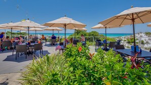 Een terras met tafels en stoelen, parasols en uitzicht op het strand.