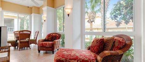 A spacious living area with wicker furniture, large windows, and a ceiling fan.