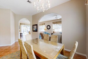 A dining area with a glass table, wicker chairs, and a chandelier. - 3BR resort home with private heated pool (Miramar Beach)