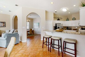 A modern kitchen with white cabinets, a granite countertop, and two bar stools. - 3BR resort home with private heated pool (Miramar Beach)