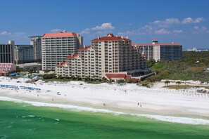 Un hotel frente a la playa con varias construcciones, una playa de arena y vista al océano.
