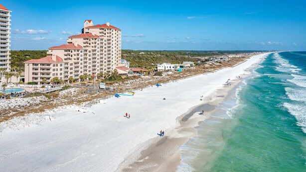 Ein Strandhotel mit mehreren Etagen, einem Sandstrand und Wellen.