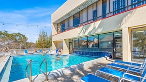 Ein Pool mit blauen Liegestühlen, ein Poolbereich und ein Gebäude mit großen Fenstern und einem Balkon.
