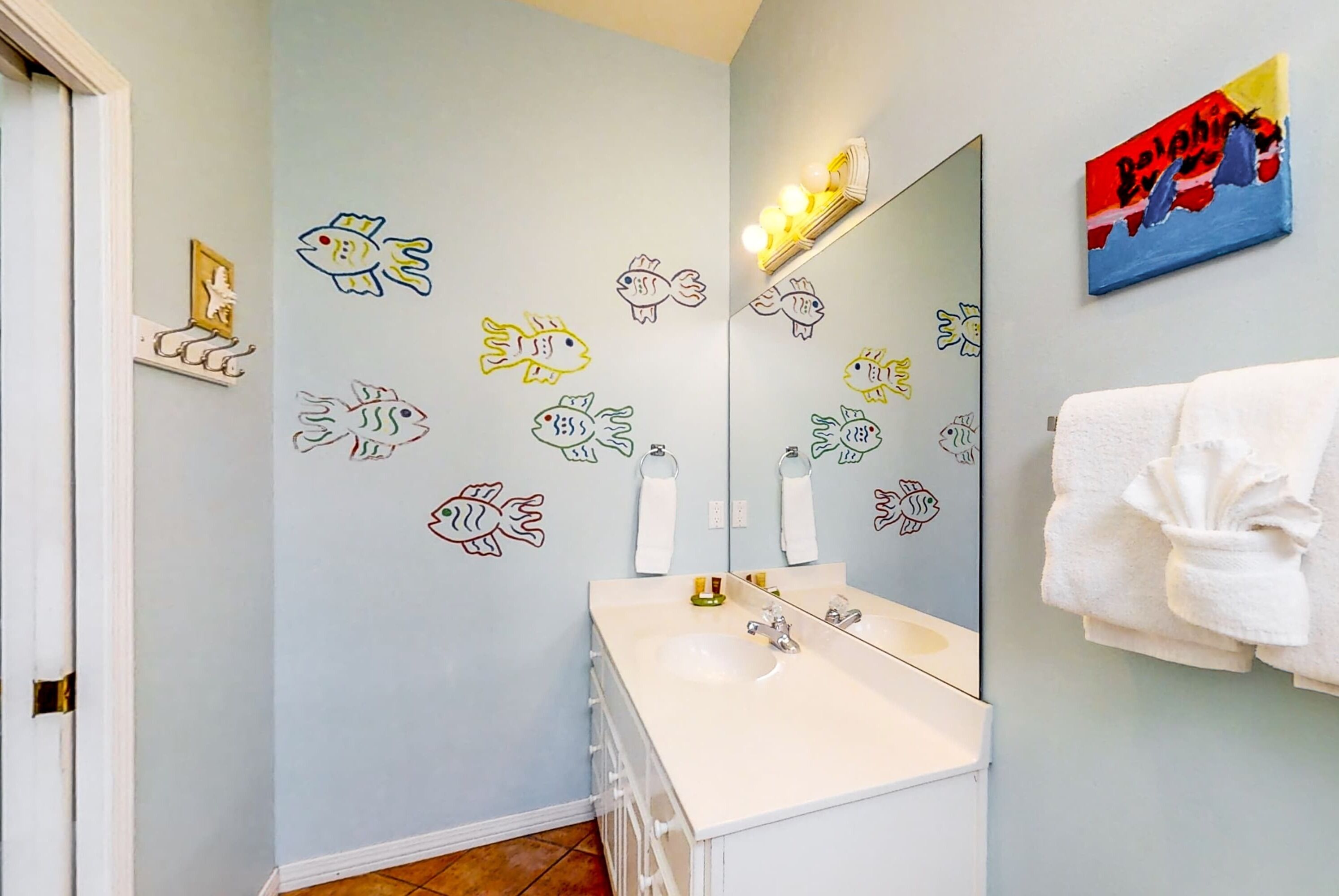A bathroom with a light blue wall, a white sink, a mirror, and fish decals.