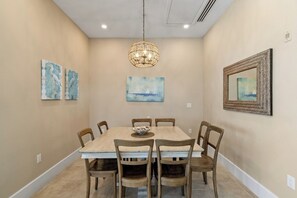 Ein Esszimmer mit einem rechteckigen Tisch, sechs Holzstühlen, einer Chandelierleuchtre und Kunstwerken an den Wänden.