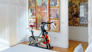 Ein Schlafzimmer mit einem Bett, einem Stehfahrrad und einer Wand mit mehreren gerahmten Kunstwerken.