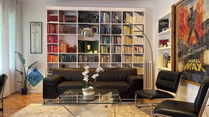 Ein Wohnzimmer mit einer schwarzen Ledersofa, einem Glastisch und einer großen Bücherwand voller Bücher.