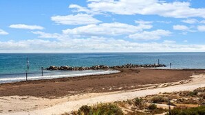 Ein Strand mit einem steinernen Wellenbrecher, blauem Himmel und ruhiger See.