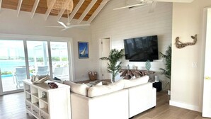 A spacious living room with a large white sectional sofa, a flat-screen TV mounted on the wall, and a wooden ceiling.