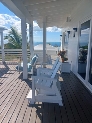 Una terraza techada con sillones blancos y una mesita, con vista a un cuerpo de agua.