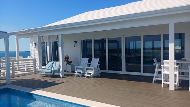 A poolside area with a view of the sea, white outdoor furniture, and a covered seating area.