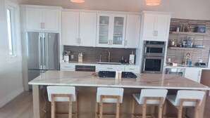 A modern kitchen with white cabinetry, a large island with bar stools, stainless steel appliances, and a striped backsplash.