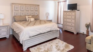A bedroom with a large bed, a dresser, a television, and a nightstand.