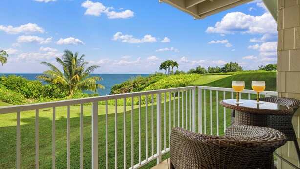 Ein Balkon mit Korbmöbeln, zwei Gläser Orangensaft und Blick auf Meer und Golfplatz.