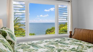 Ein Schlafzimmer mit einem großen Fenster und Meer- sowie Grünblick.