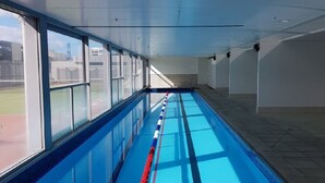 Ein langer, überdachter Schwimmbereich mit deutlichen Bahnen, großen Fenstern an einer Seite und einem gefliesten Boden.