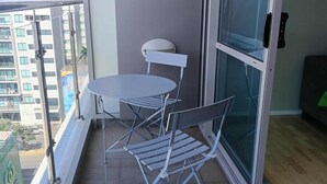 Ein Balkon mit Tisch und Stühlen, eine Schiebetür und Blick auf eine Stadtlandschaft.