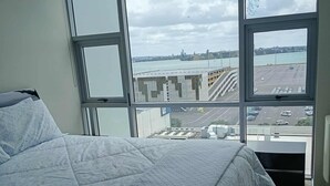 Ein Schlafzimmer mit einem großen Bett, einem Fenster mit Blick auf einen Parkplatz und Gebäude sowie einer Heizung.