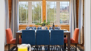 Een eetruimte met een houten tafel gedekt voor vier personen, blauwe stoelen en een vaas met bloemen.