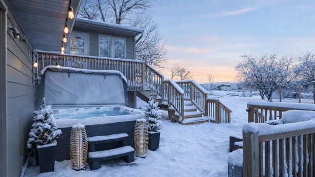 Een besneeuwde buitenruimte met een jacuzzi, houten trappen en een terras.