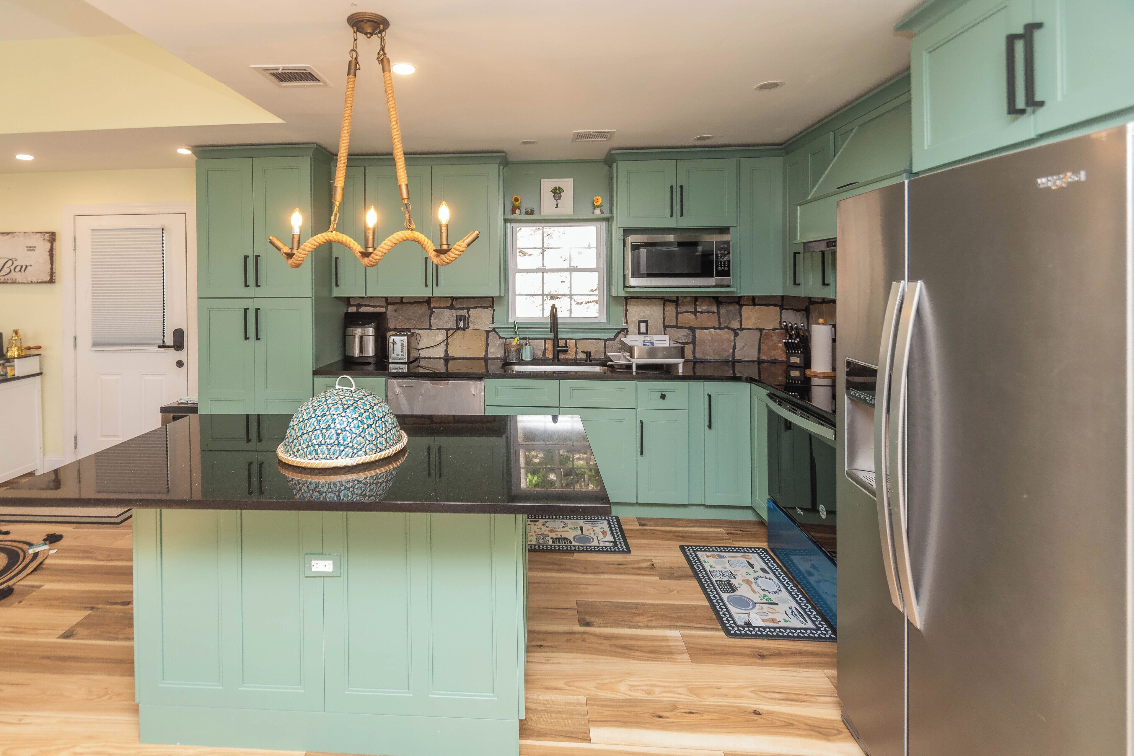 Une cuisine avec des meubles de couleur turquoise, un îlot central, un réfrigérateur en acier inoxydable et un luminaire suspendu.