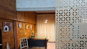 A room with wooden walls, a dining table with chairs, a decorative plant, and a patterned wall divider. - Renovated house • Air conditi• Garage • BR-116 • Route to the beaches of SC (Guaíba)