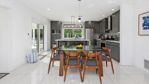 Una cocina moderna con una isla central, armarios grises, electrodomésticos de acero inoxidable y un amplio ventanal con vistas a zonas verdes.