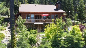 Eine Lodge mit steinernen Fundament, einer Holzterrasse und einem großen Fenster mit Blick auf einen bewaldeten Bereich.