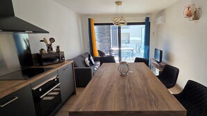 A modern kitchen with a built-in stove, a dining table with chairs, and a view of a balcony with blue curtains. - Nice and cozy T2, near beaches, Terra Doru B02 (Propriano)