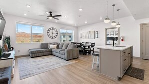 A spacious living area with a large window, a ceiling fan, a dining table, and a kitchen island. - Red Rock Haven at Terra Resort | Sage Vacations (Hurricane)