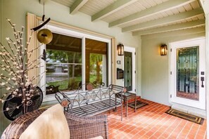 A covered porch with a bench, a wicker chair, and a decorative plant arrangement. - Bnb Hyperion Newly Remodeled 1B Home w Patio (Hollywood)