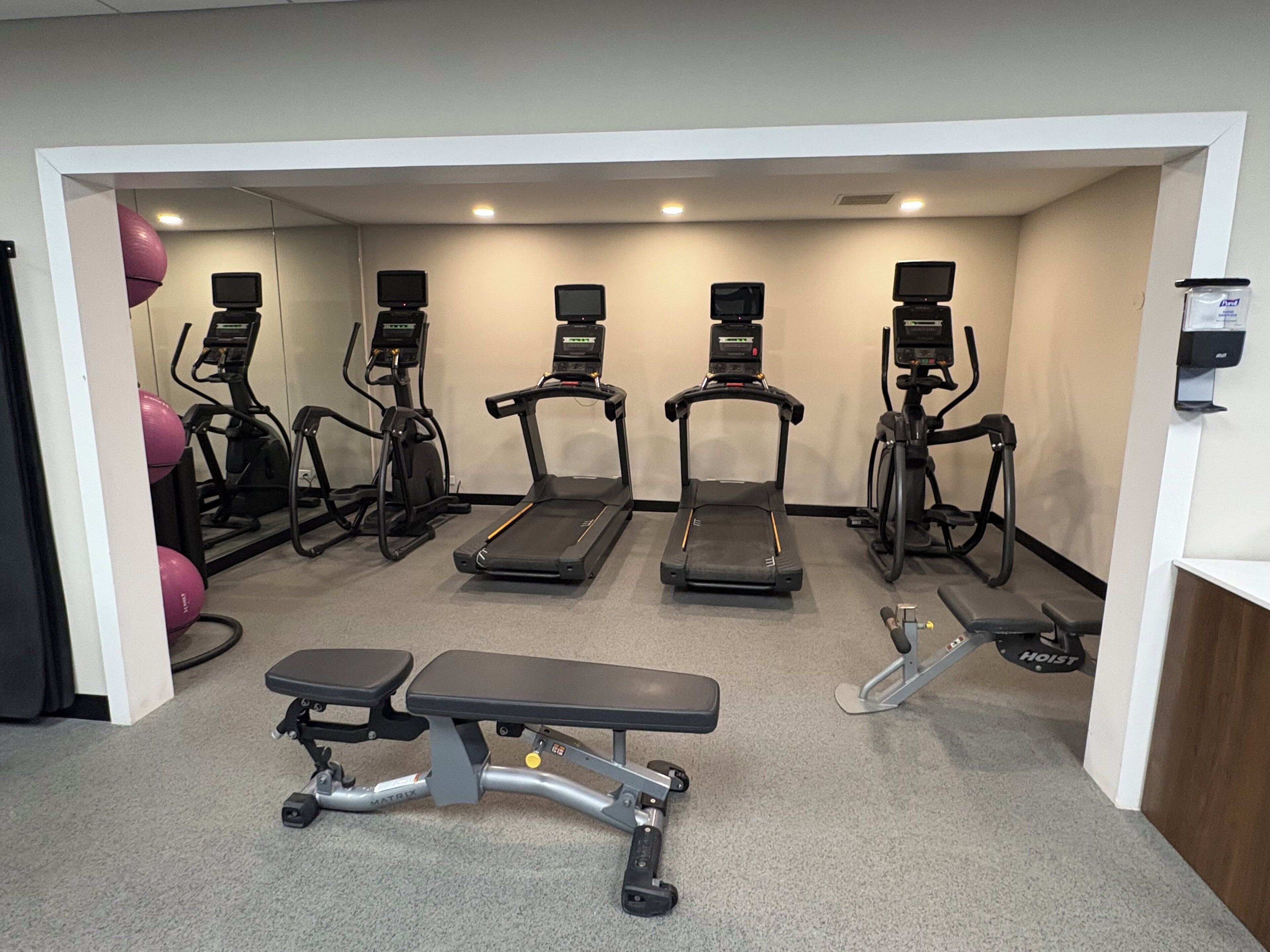 A gym with treadmills, elliptical machines, and a bench.