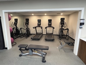 Un gimnasio con cintas de correr, elípticas y una banca.