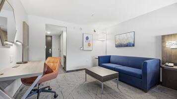 A modern hotel room with a desk, chair, sofa, and a small coffee table.