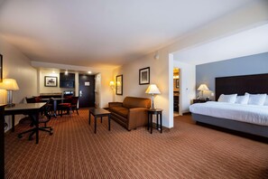 A hotel room with a bed, a desk, a sofa, and a small table. There are lamps on both sides of the room. - Holiday Inn Express & Suites RALEIGH WEST - LENOVO CENTER by IHG (Meredith)